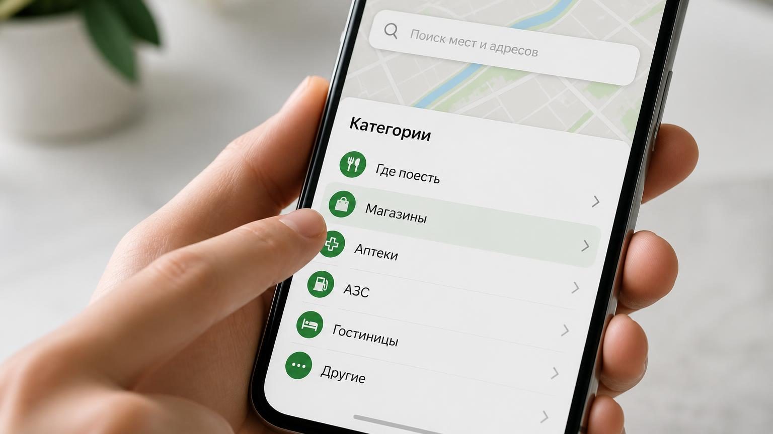 Экран смартфона с открытым списком категорий в картографическом приложении, палец занесён над одной из рубрик. Крупный план, естественный свет.